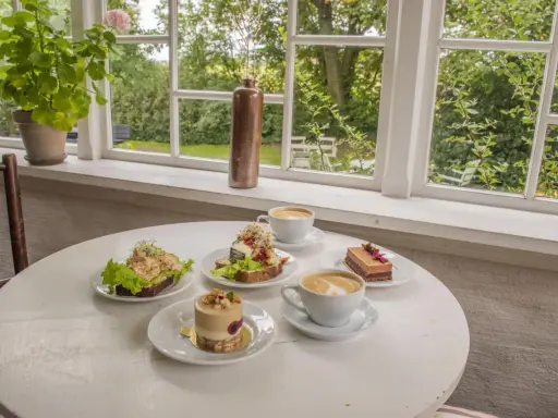 Fika på ett mysigt cafe i Skåne med smörgåsar, tårtor och kaffe.