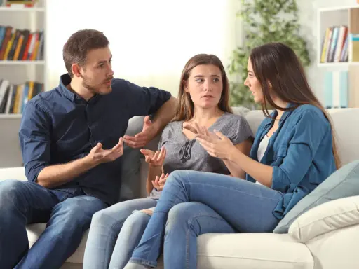 Tres personas sentadas en un sofá blanco discuten animadamente, gesticulando con las manos, en un intento por resolver conflictos.