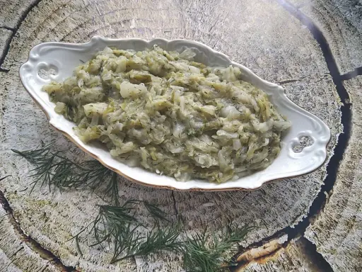 Pyszna kapusta zasmażana z koperkiem, podana w ozdobnej misie na tle drewnianej tekstury.