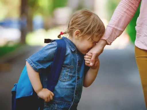 Niña con mochila azul llora y se aferra a la mano de su madre. Parece que mi hija no quiere ir al colegio.