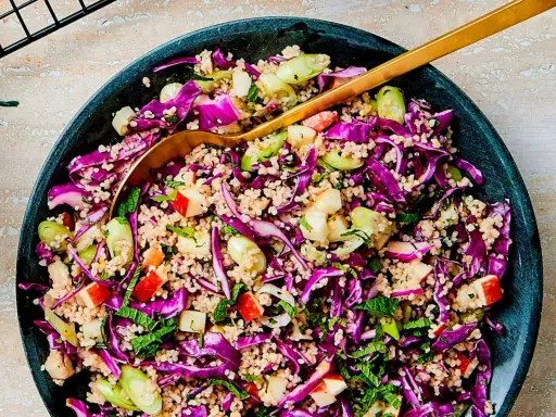En färgglad couscous sallad med rödkål, äpple och mynta. En gyllene sked vilar i den fräscha rätten.