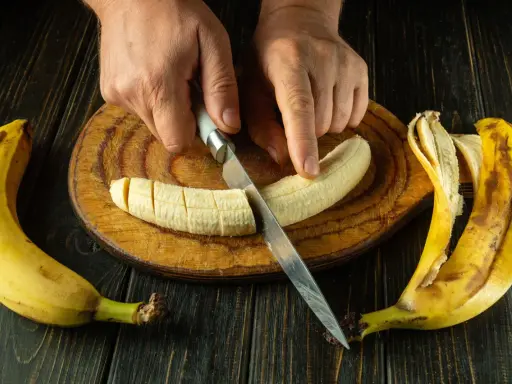 Dłonie kroją banana na desce. To świetny pomysł, co jeść na skurcze nóg, bo banany są bogate w potas.