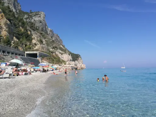 Varigotti spiaggia più bella: gente rilassata sotto gli ombrelloni, mare cristallino e scogliere imponenti.