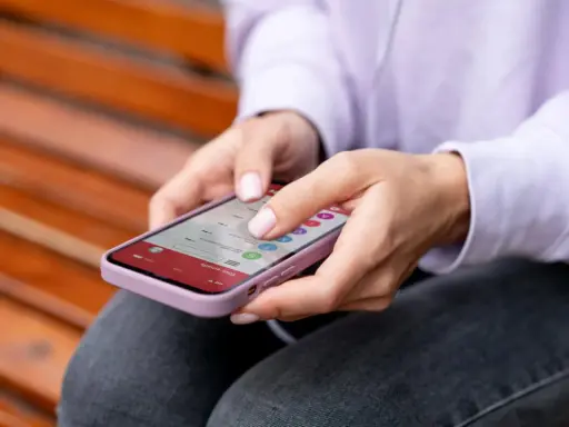 Dłonie kobiety obsługują smartfon, który wyświetla listę e-maili. To przykład interakcji, która może wykorzystywać haptykę – co to za technologia?