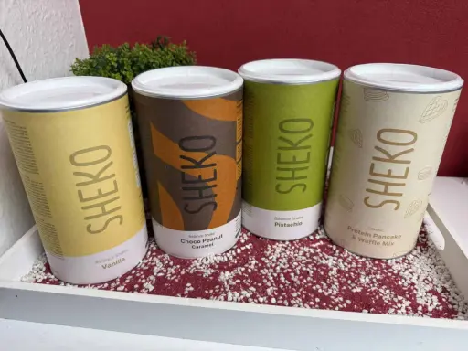 Vier Dosen SHEKO mit verschiedenen Geschmacksrichtungen: Vanille, Choco Peanut Caramel, Pistachio und Protein Pancake & Waffle Mix. Perfekt für einen schnellen Shake mit Wasser.