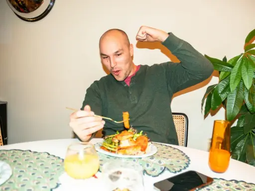 Mann feiert sein **Essen nach Marathon** mit einem kräftigen Bizeps-Zeigen und einem Bissen vom Teller.