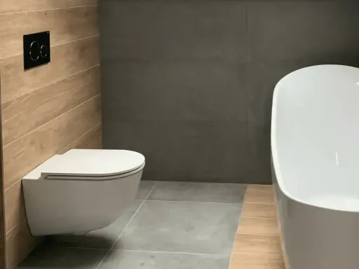 Salle de bain moderne avec un élégant **pose wc suspendu** sur un mur en bois, face à une baignoire blanche et des murs gris.