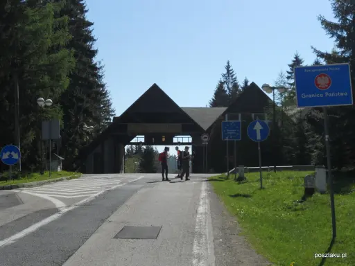 Przejście graniczne na Pilsku. Znaki drogowe i budynek z napisem "Wyciągi Narciarskie". Szlaki górskie w tle.
