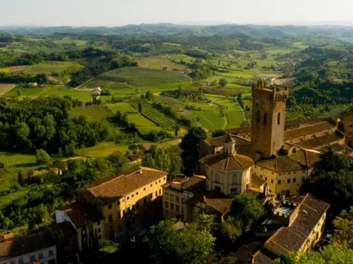 Un borgo medievale con una torre svetta tra le verdi colline pisane, un paesaggio da cartolina.