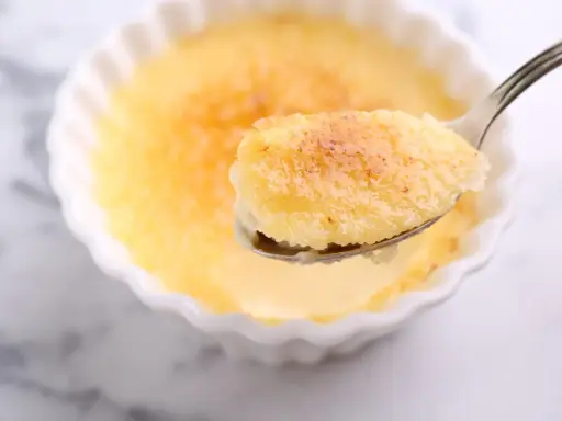 Une cuillère de semoule au lait et aux œufs, avec sa croûte caramélisée dorée, prête à être dégustée.