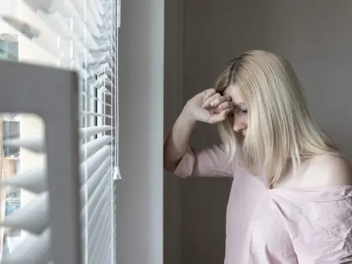 Mujer rubia con la mano en la frente, mirando hacia abajo, con un aire de melancolía que evoca el síndrome de Wendy.