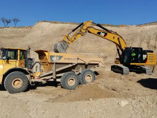 Excavadora CAT cargando volquete Volvo en obra de movimiento de tierras.