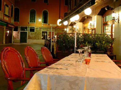 Table dressée devant la trattoria "da Roberto" à Venise, avec des chaises rouges et des verres à vin.
