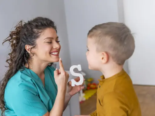 Logopeda pomaga dziecku z dyslalią ćwiczyć wymowę litery "S", używając białej literki.