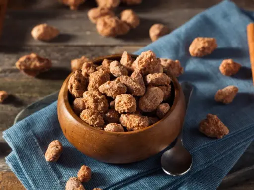 Schüssel mit gebrannten Mandeln, Zimtstangen und Löffel. Ein süßer Snack, der auch in der Schwangerschaft genossen werden kann.