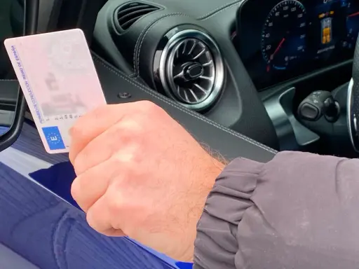 Mano sujetando permiso de conducir español dentro de un coche moderno, anticipando la conducción autónoma en España.