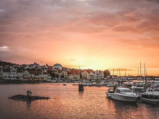 En pittoresk svensk kuststad vid solnedgången, med båtar i hamnen och hus längs vattnet. En perfekt plats för upplevelser i Sverige.