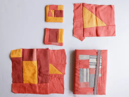 Kilka fragmentów tkanin w odcieniach koralu i żółci, tworzących wzory geometryczne. To jest właśnie patchwork – sztuka łączenia skrawków materiału.