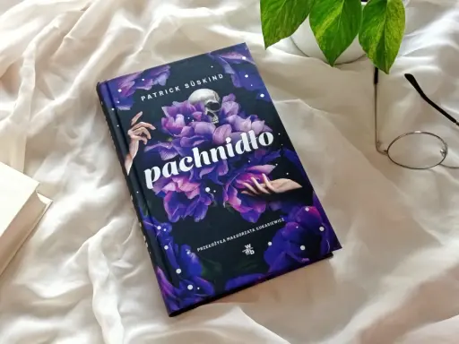 Powieść Patricka Süskinda "Pachnidło" na tle białej tkaniny, obok okularów i innej książki.
