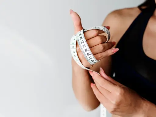 Kobieta z miarką w dłoni, symbolizującą kontrolę nad wagą i dążenie do idealnego BMI.