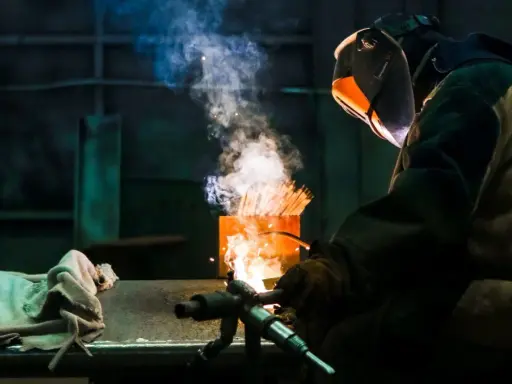 Soldador usa un electrodo rutilo para crear uniones fuertes. El humo y las chispas iluminan la escena industrial.