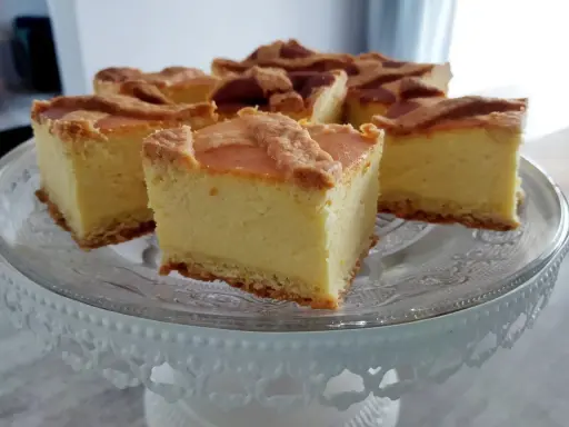 Pyszny sernik na kruchym spodzie, pokrojony na kwadraty, prezentuje się apetycznie na szklanej paterze.