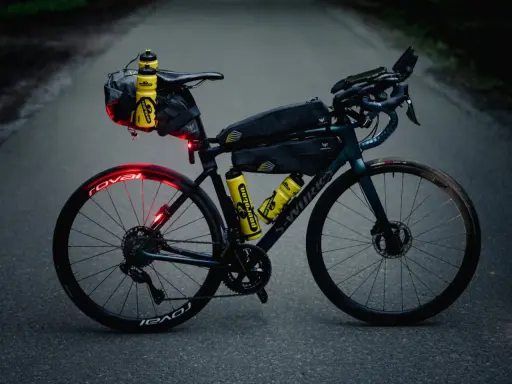 Bereit für ultra cycling: Rennrad mit Bikepacking-Taschen, Trinkflaschen und Lichtern auf asphaltierter Straße.