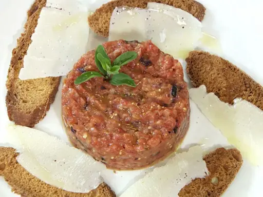 Delicioso tartar de tomate fresco, servido con finas láminas de queso y tostadas crujientes.