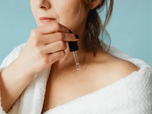 Une femme applique un sérum à base de peptide sur sa peau, enveloppée dans un peignoir blanc douillet.