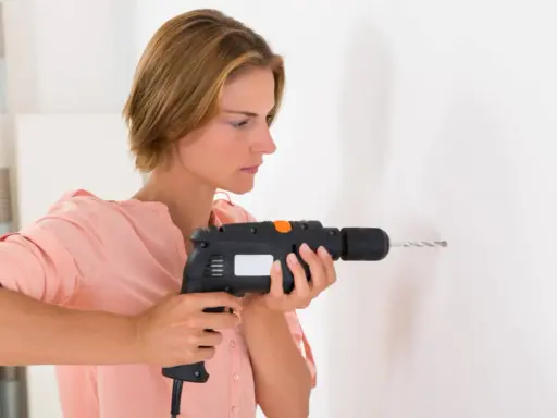 Mujer usando un taladro, mostrando sus partes como el gatillo y la broca, para hacer un agujero en la pared.