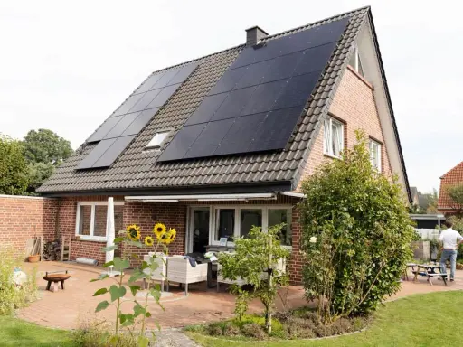 Tak på ett tegelhus med solceller som ger hög verkningsgrad. Solrosor blommar på uteplatsen.
