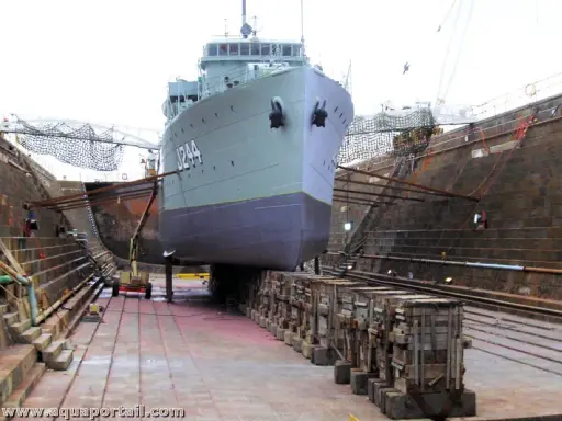Un grand navire est en cale sèche, soutenu par des structures en bois. Le support bateau cale sèche est essentiel pour les réparations.