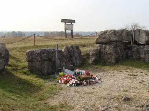 Pomnik na Górze Strękowej z krzyżem i wieńcami. W tle widoczne bunkry i krajobraz.