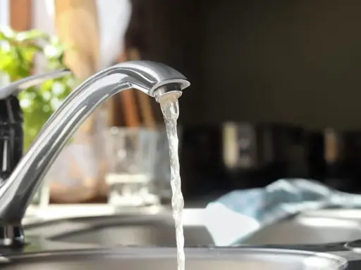 Wasserhahn mit integriertem Durchlauferhitzer, Testsieger. Wasser fließt aus dem Hahn in die Spüle.