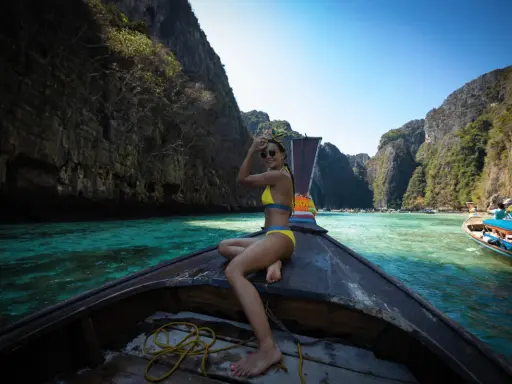 Kobieta w bikini na łodzi, podróżująca po turkusowej wodzie między klifami. Idealne miejsce na wakacje na własną rękę.