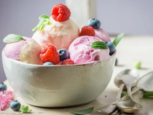 Deliciosos helados caseros de fresa y vainilla, adornados con frambuesas y arándanos frescos.