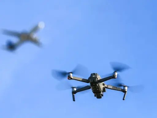 Drohne im Flug, während ein Flugzeug im Hintergrund verschwimmt. Informiere dich über Länder, in welchen Ländern Drohnen verboten sind, bevor du abhebst.