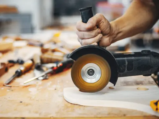 Mano trabajando con amoladora, mostrando sus usos en carpintería para dar forma a la madera.