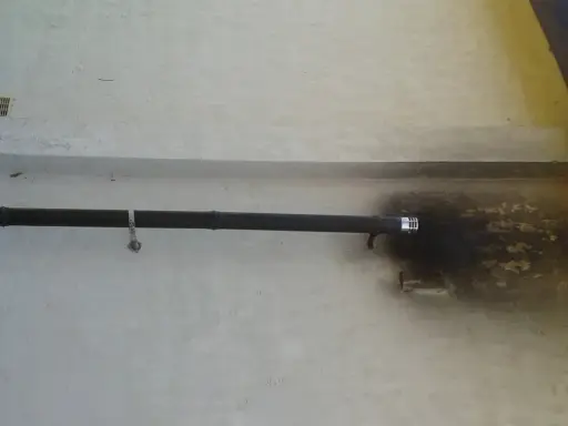 Tuyau d'évacuation noir d'un poêle à pellet ventouse, fixé au mur blanc, avec des traces de suie autour de la sortie.