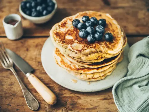 Pile de pancakes au levain garnis de myrtilles, sur une assiette, avec une fourchette et un couteau.