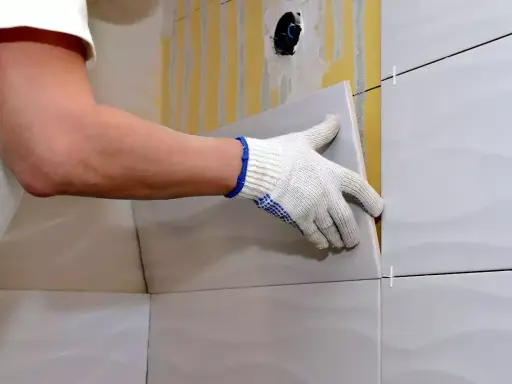 Man con guantes coloca una baldosa nueva sobre un alicatado existente.