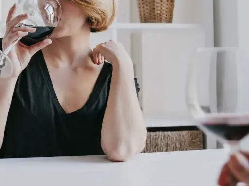 Kobieta z krótkimi blond włosami pije czerwone wino. Czy zastanawiasz się, jak hashimoto a alkohol wpływają na zdrowie?