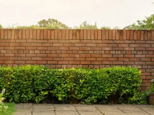 Eine Ziegelmauer im Garten, umgeben von üppigem Grün und blühenden Pflanzen. Tolle Ideen für Gartenmauern!