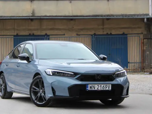 Nowy Honda Civic 11. generacji w szarym kolorze prezentuje się elegancko na tle industrialnego krajobrazu.