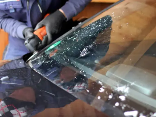 Rękawiczki i narzędzie pracują nad usunięciem odprysku na szybie samochodu.