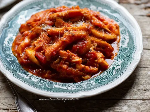 Un piatto fumante di trippa alla romana, ricca di sugo di pomodoro e condita con pecorino grattugiato, servita su un piatto decorato.