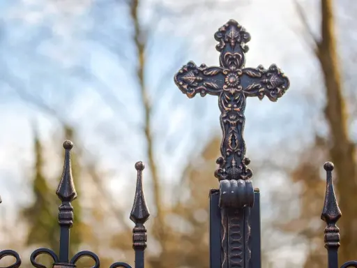 Krzyż na metalowym ogrodzeniu, symbol nadziei i walki z siedmioma grzechami głównymi.