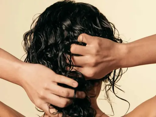 Manos peinando cabello oscuro y rizado, con un toque de cabello esponjado.