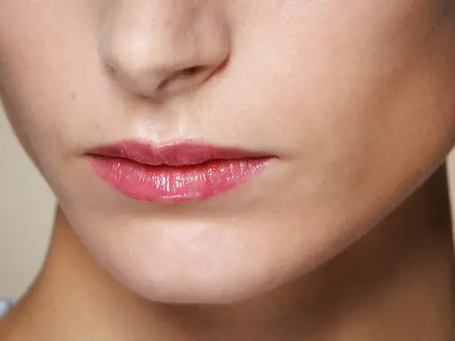 Labbra sottili e lucide con un tocco di gloss rosa, che catturano la luce.