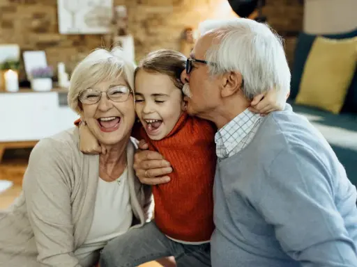 Una niña ríe mientras su abuelo le da un beso y su abuela la abraza. Así de felices los abuelos son.